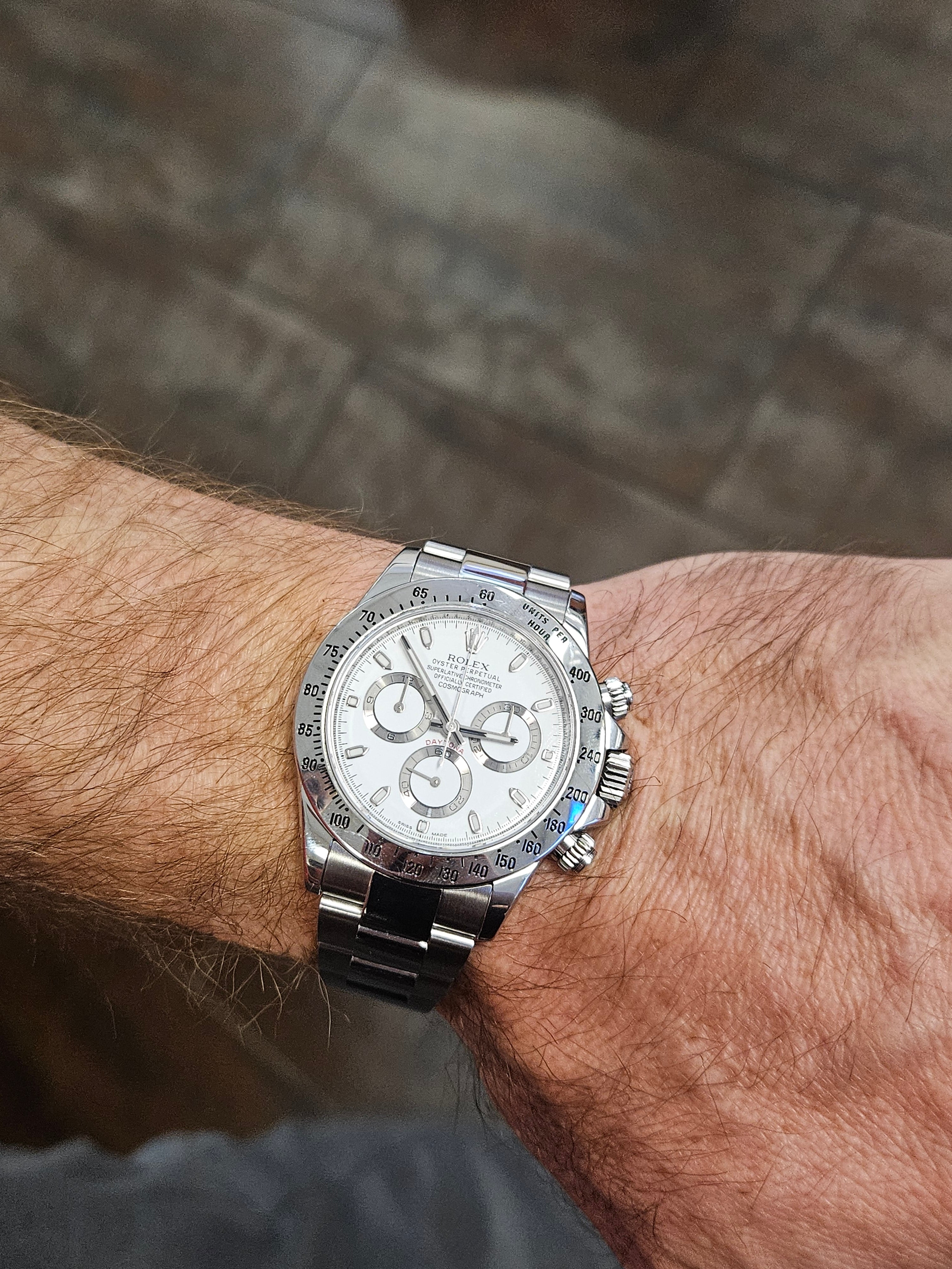Rolex Daytona stainless steel chronograph watch on wrist with white dial and silver bracelet